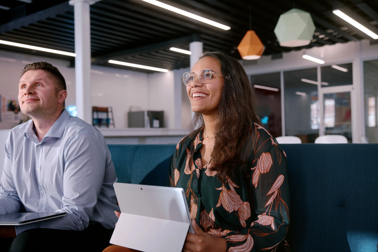 A smiling woman sitting behind a counter with an open laptop in front of her.